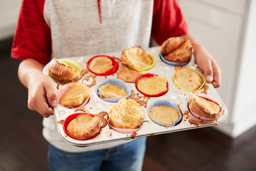Boy holding baking tray, presenting the cakes he has baked to camera, mid section, close up