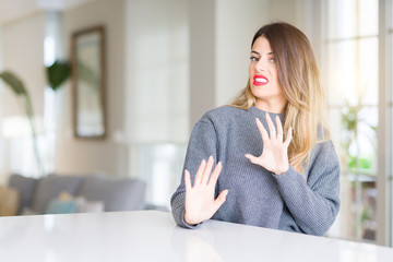 Obraz premium Young beautiful woman wearing winter sweater at home disgusted expression, displeased and fearful doing disgust face because aversion reaction. With hands raised. Annoying concept.