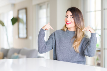 Young beautiful woman wearing winter sweater at home looking confident with smile on face, pointing oneself with fingers proud and happy.