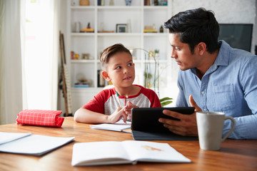 Hispanic pre-teen boy sitting at dining room table working with his home school tutor