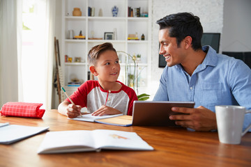 Hispanic pre-teen boy sitting at table working with his home school tutor, smiling at each other