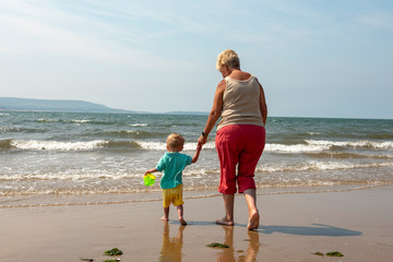 Grandmother and two year old grandson walking along the beach 