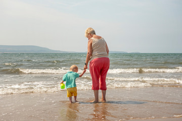 Grandmother and two year old grandson walking along the beach 