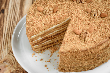Homemade sweet layered honey cake with nuts on white plate on wooden table with bowl of honey, cinammon and badian.
