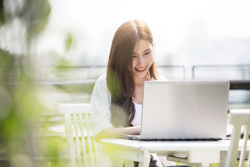 Young and beautiful Asian woman talking on mobile phone and working with her laptop while sitting on the steps outside the modern office building in the urban city