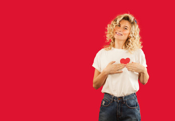young emotional girl with a red heart in her hands is standing on an isolated red background. Lovers day concept,Valentine's Day.