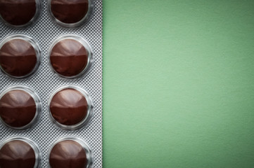 Blister with brown tablets on a green background.