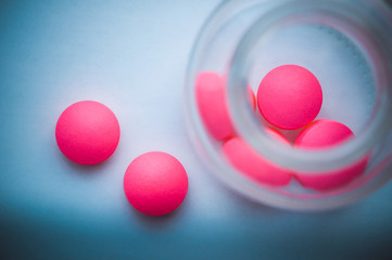 Pink pills are poured from a glass jar on a white blue background. The view from the top.