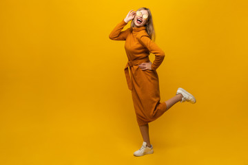 Full length portrait of a cheerful beautiful girl wearing dress having fun and dancing isolated over yellow background. - obrazy, fototapety, plakaty