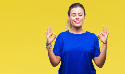 Young beautiful woman wearing casual blue t-shirt over isolated background relax and smiling with eyes closed doing meditation gesture with fingers. Yoga concept.