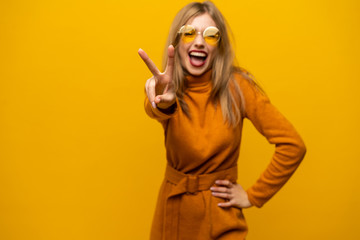 Image of happy young woman standing isolated over yellow background showing peace gesture. Looking camera