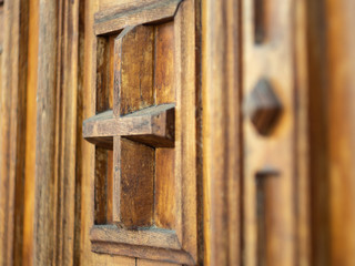 Fragment of brown wooden door in monastery, close up view. Door with cross and decorative carvings. Ancient wooden door in monastery, Ukraine. Ornate gate. Blurred background. Selective soft focus