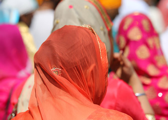 woman with head covered by a colorful orange veil during an outdoor parade