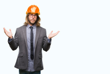 Young handsome architec man with long hair wearing safety helmet over isolated background clueless...