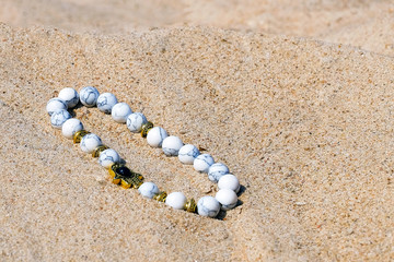 Bracelet of lapis lazuli on the sand. White round beads on thread. Top view close-up.