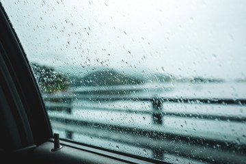 Driving a car in a dodgy weather. Dodge drops on the car window. View of the fjord through a wet window in the rain