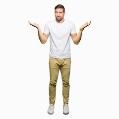 Handsome man wearing casual white t-shirt clueless and confused expression with arms and hands...