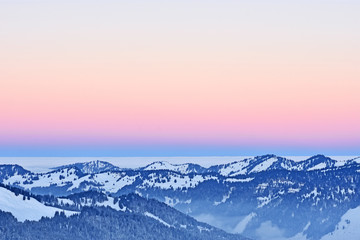 Naklejka na ściany i meble Forested hill country at a cold winter day in the Allgaeu Alps (Bavaria, Germany). Dawn with blue and red illuminated sky. Copy space.