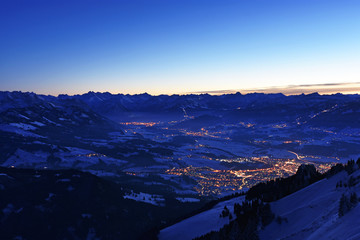 City night lights of Sonthofen and Oberstdorf (Allgaeu Alps, Bavaria, Germany) after sunset from the summit of Gruenten mountain in winter. Alpine landscape during blue hour. Copy space.