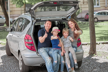 Fototapeta na wymiar family sitting in the trunk of a family car and showing thumbs up