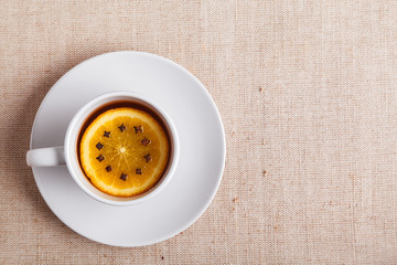 Tea break concept. A Cup of warming tea with orange and cloves. English concept of tea time. A Cup of tea with pieces of citrus makes a cozy composition, top view