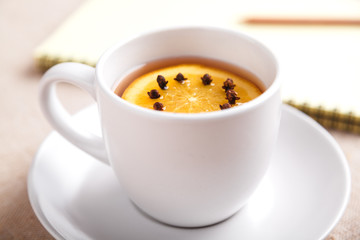 A Cup of tea with a piece of orange and cloves next to a pencil and a notebook on a table covered with a linen tablecloth, write down the list of actions. Concept of planning. Top view, copy space