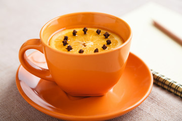 A Cup of tea with a piece of orange and cloves next to a pencil and a notebook on a table covered with a linen tablecloth, write down the list of actions. Concept of planning. Top view, copy space