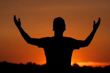 Silhouette of man clamoring to the heavens, sunset background.