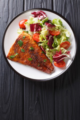 Serve baked pike fillet and fresh salad close-up on a wooden table. Vertical top view