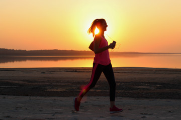 Fototapeta na wymiar Young beautiful woman is running along the seashore on the orange sunset background