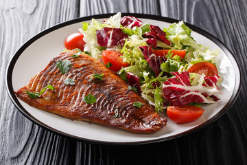 Serve baked pike fillet and fresh salad close-up on a wooden table. horizontal