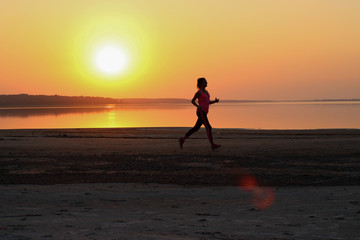Young beautiful woman is running along the seashore on the orange sunset background
