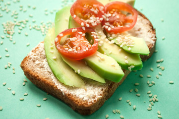 Delicious toasts with sliced avocado, tomatoes and sesamum seeds on blue background with copyspace....