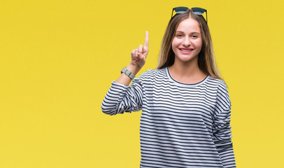 Young beautiful blonde woman wearing sunglasses over isolated background showing and pointing up with finger number one while smiling confident and happy.