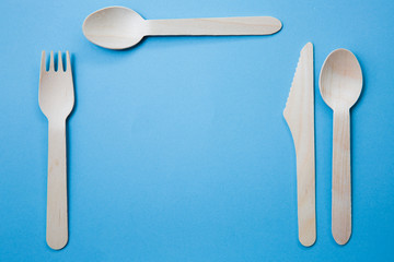 An Assortment of Wooden Cutlery arranged in a place setting ready for a meal on blue background with copy space