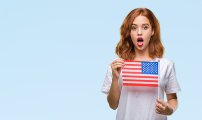 Young beautiful woman holding flag of america over isolated background scared in shock with a surprise face, afraid and excited with fear expression