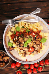 Penne pasta rigatoni in tomato sauce with mushrooms, tomatoes decorated with parsley and basil