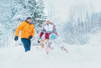 Fototapeta na wymiar Mother and father family fooling in snow forest by throwing their little daugher to snowdrift