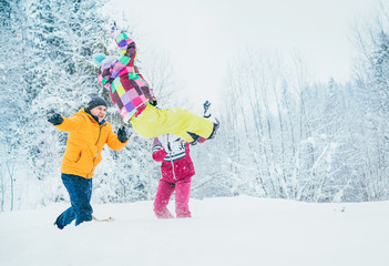 Mother and father family fooling in snow forest by throwing their little daugher to snowdrift