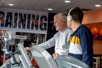 Fototapeta na wymiar Senior man and young man running on a treadmill in the gym