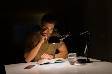 Young handsome man studying at home, reading a book at night