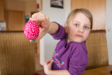 Ein 7 jahre altes Mädchen lächelt und hält ein rotes gepunktetes Osterei in die Kamera