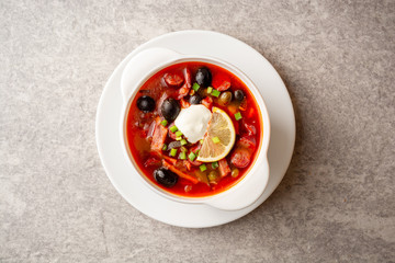 Traditional Russian meat soup Solyanka in bowl on grey stone background. Top view. Copy space.