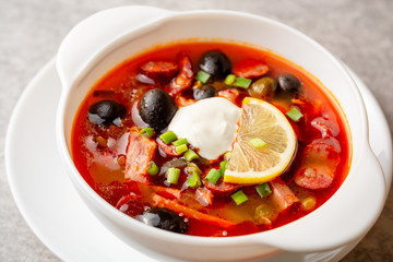 Traditional Russian meat soup Solyanka in bowl on grey stone background. Selective focus.