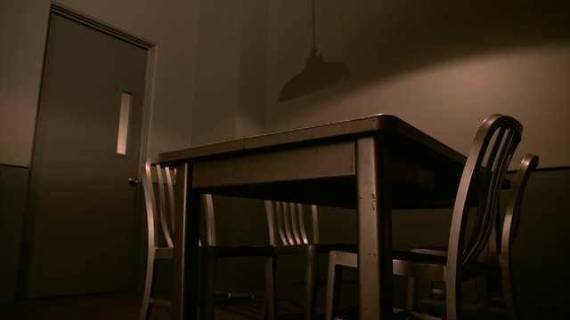 VERY LOW ANGLE OF AN EMPTY INTERROGATION ROOM WITH CHINA HAT LIGHT GENTLY SWAYING.  4K.