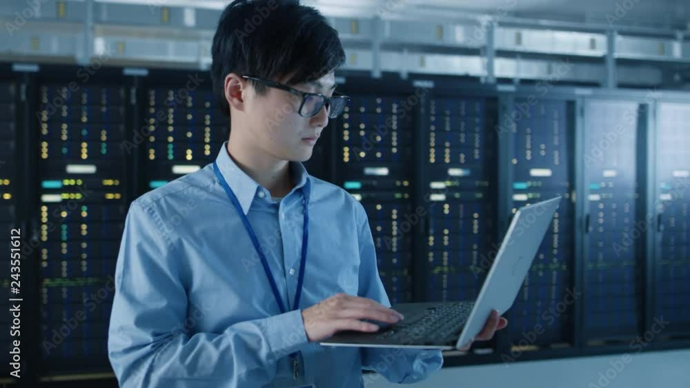 Poster  In the Modern Data Center: Portrait of IT Engineer Standing with Server Racks Behind Him, Doing Maintenance and Diagnostics Procedure Using Laptop. Arc Camera Shot.
