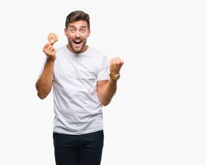 Young handsome man eating chocolate chips cookie over isolated background screaming proud and celebrating victory and success very excited, cheering emotion