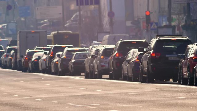 Blurred street shot of cars standing in traffic jam and slowly moving on city background.