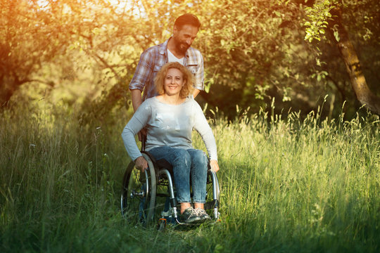 Smiling woman in wheelchair with husband in the park on sunny day