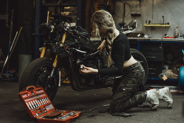 Obraz na płótnie Canvas beautiful girl with long hair in the garage repairing a motorcycle